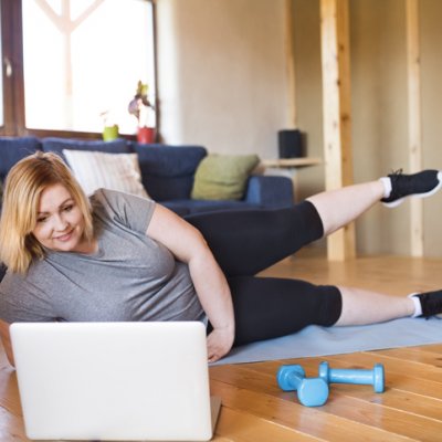 woman in exercise gear lying on a yoga mat in front of a lap top, doing scissor kicks